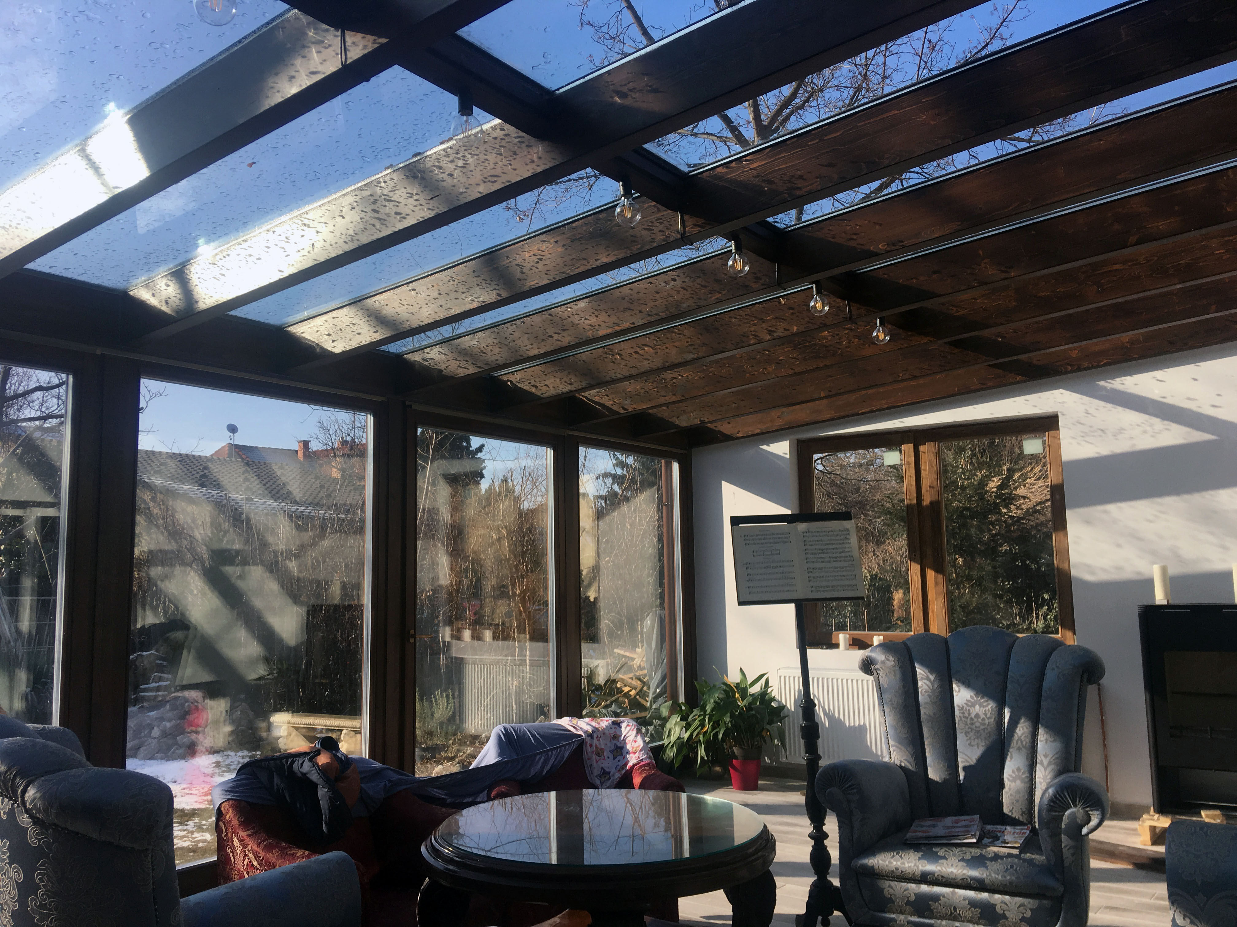 Barna fa hatású télikert belső tere nagy üvegfelülettel tolóajtóval ülőgarnitúrával nyáron