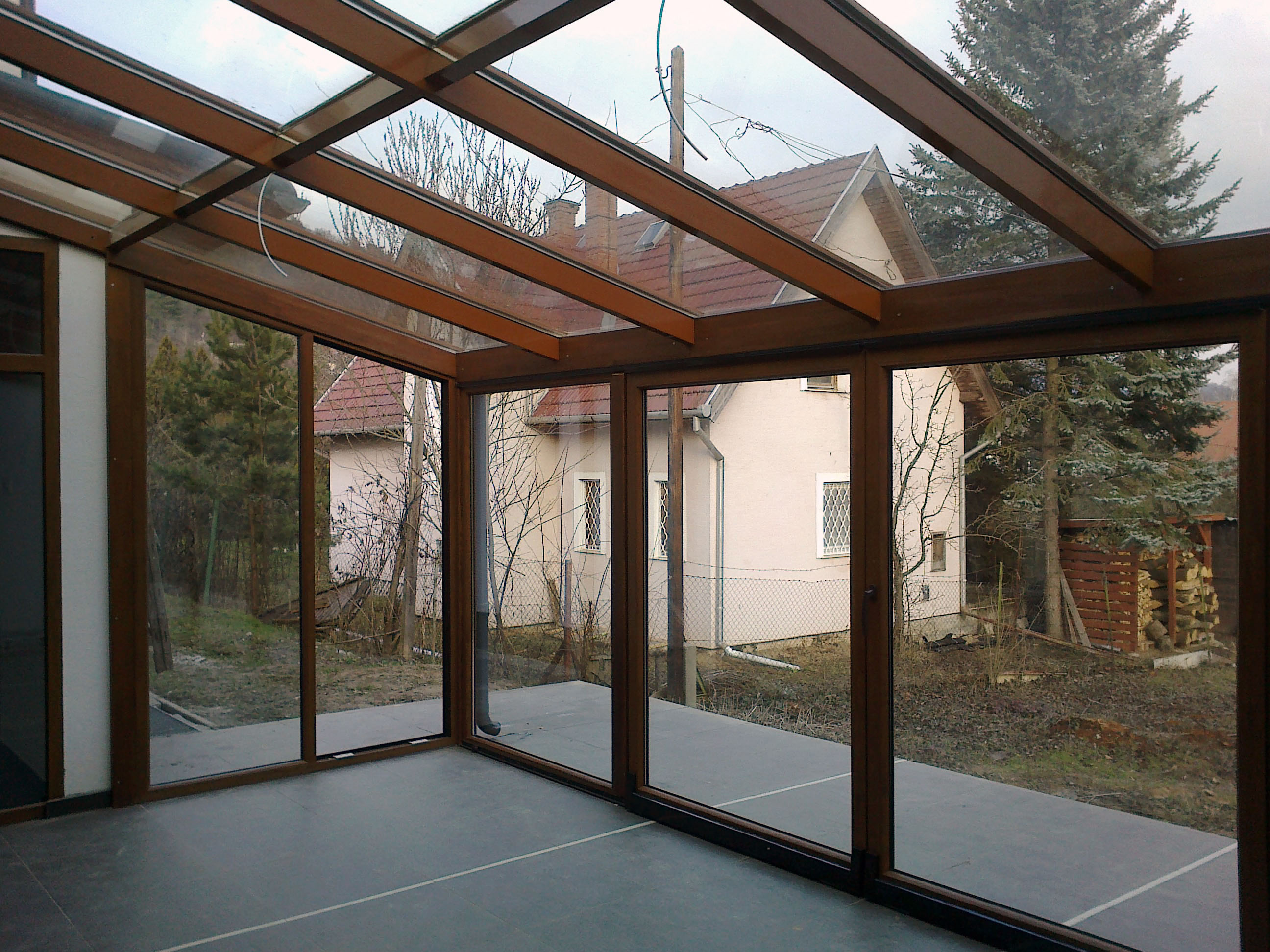 Modern barna fa hatású télikert belső tere nagy üvegfelülettel tolóajtóval üresen