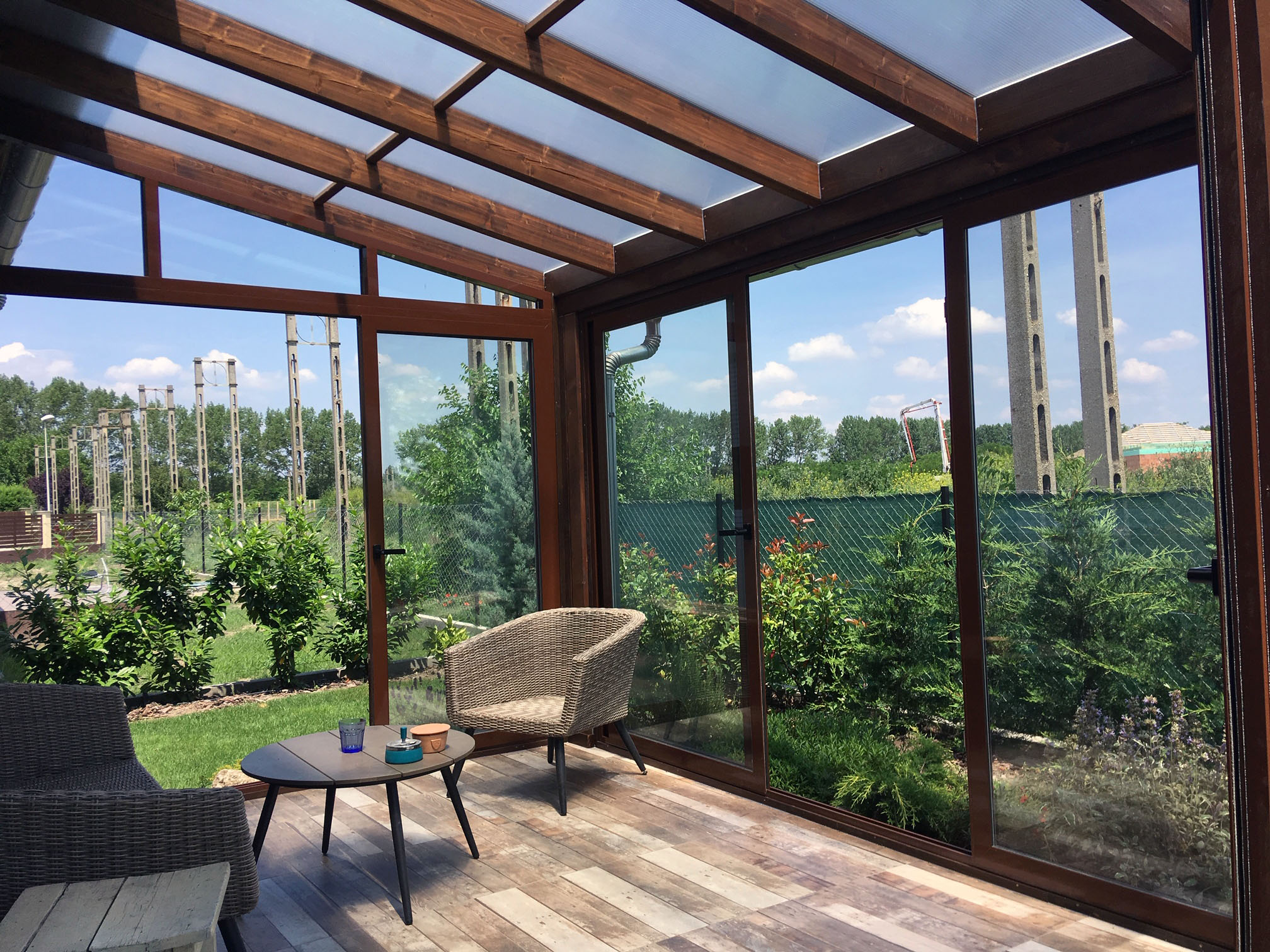 Modetn fa hatású barna télikert belső tere nagy üvegfelülettel tolóajtóval és két székkel