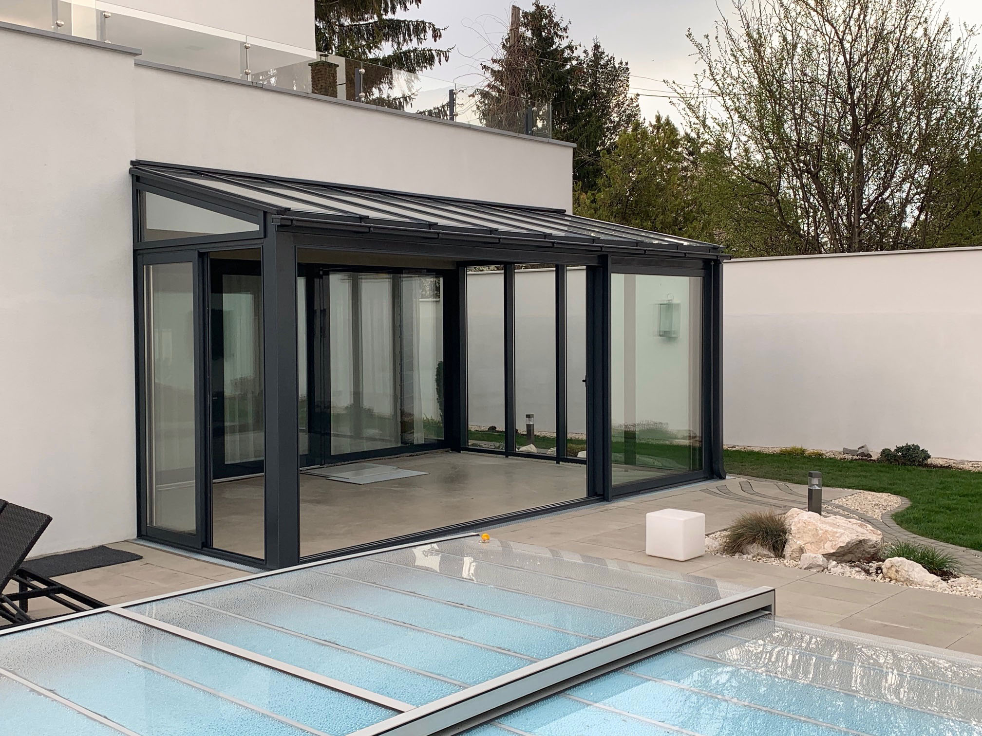 Modern szürke télikert nagy üvegfelülettel tolóajtóval családi házhoz kapcsolva